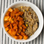 White bowl of creamy millet porridge topped with vibrant diced mangoes and sprinkled with crushed pistachios, served on a striped tablecloth.