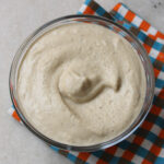 A bowl of smooth and creamy cashew cheese dip placed on a colorful napkin.