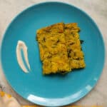 Top view of savory baked chickpea pancakes with zucchini and moringa, served on a blue plate with a dollop of sauce.