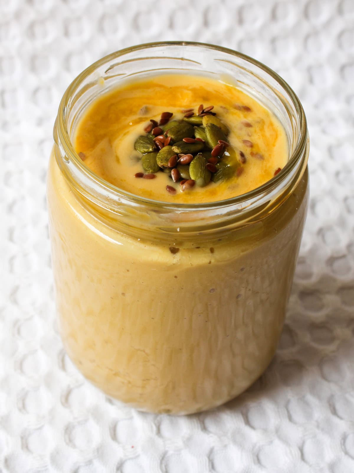 Glass jar filled with thick mango protein smoothie, swirled and topped with seeds.