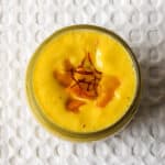 Creamy mango lassi smoothie in a glass jar, topped with saffron strands and mango chunks.