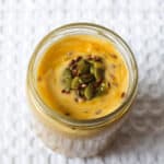 Top view of a creamy mango protein smoothie topped with pumpkin and flax seeds.