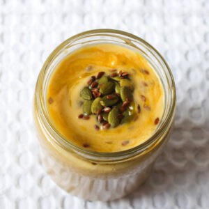 Top view of a creamy mango protein smoothie topped with pumpkin and flax seeds.