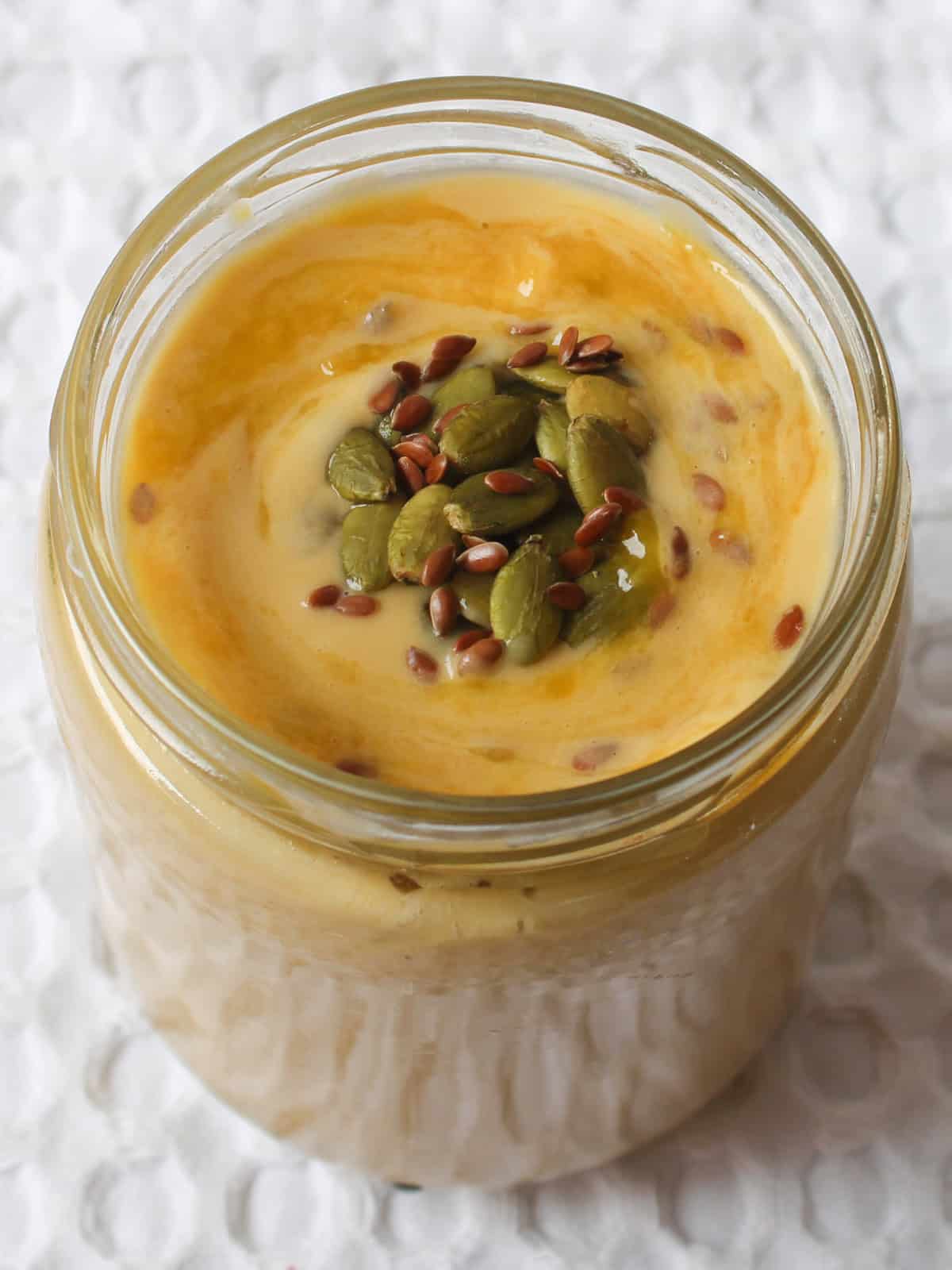 Close-up of mango smoothie with visible pumpkin and flax seeds on top.