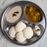 South Indian breakfast plate with idli, ridge gourd sambar, peanut chutney, and coconut chutney served on a stainless steel plate.