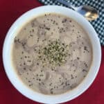 A creamy apple tahini smoothie topped with chia and hemp seeds, served in a white bowl on a red cloth.